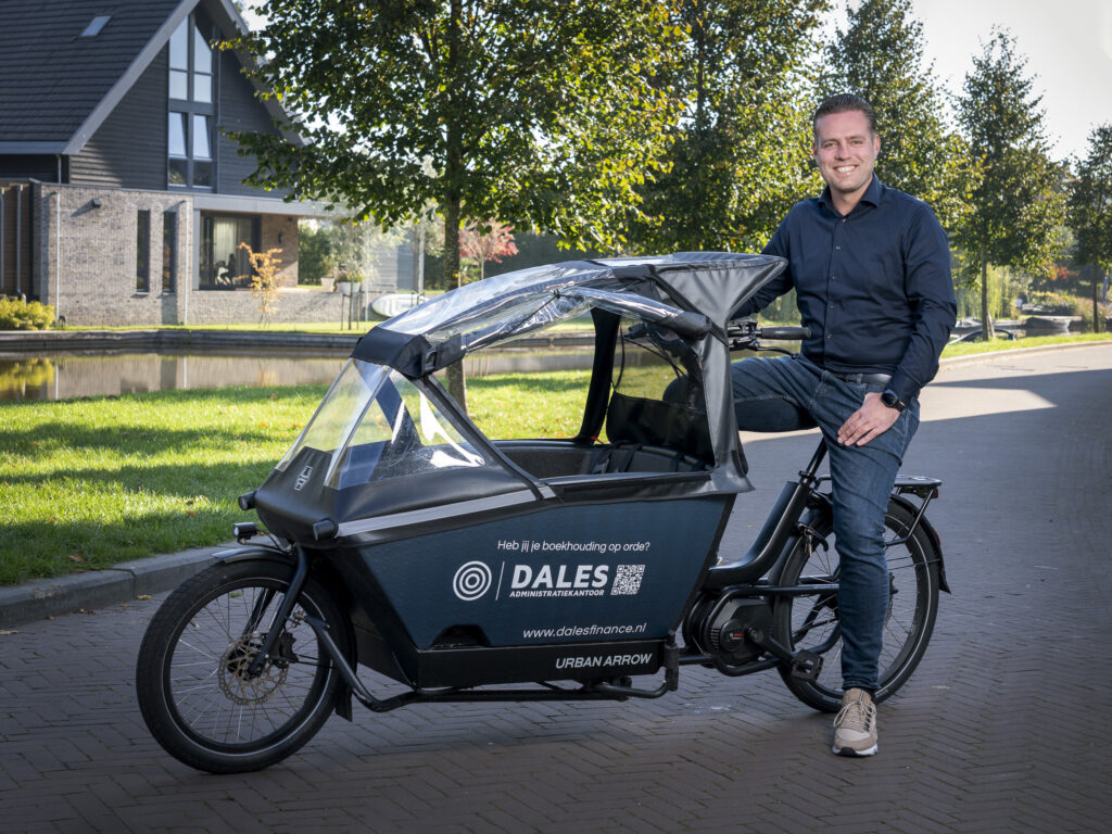 2025_Jorn Dales031 Jorn, eigenaar van Dales Finance, zit lachend op het zadel van een bakfiets. Op de bakfiets staat de tekst: ‘Heb jij je boekhouding op orde? Dales Administratiekantoor.’ De foto straalt toegankelijkheid en deskundigheid uit.